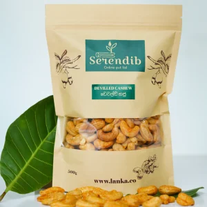 A bag of deviled cashew nuts with some loose nuts and a green leaf beside it.
